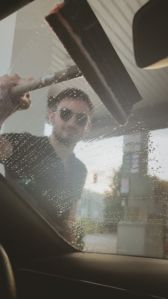 about-05 A man in sunglasses washes a car window at a gas station using a squeegee.