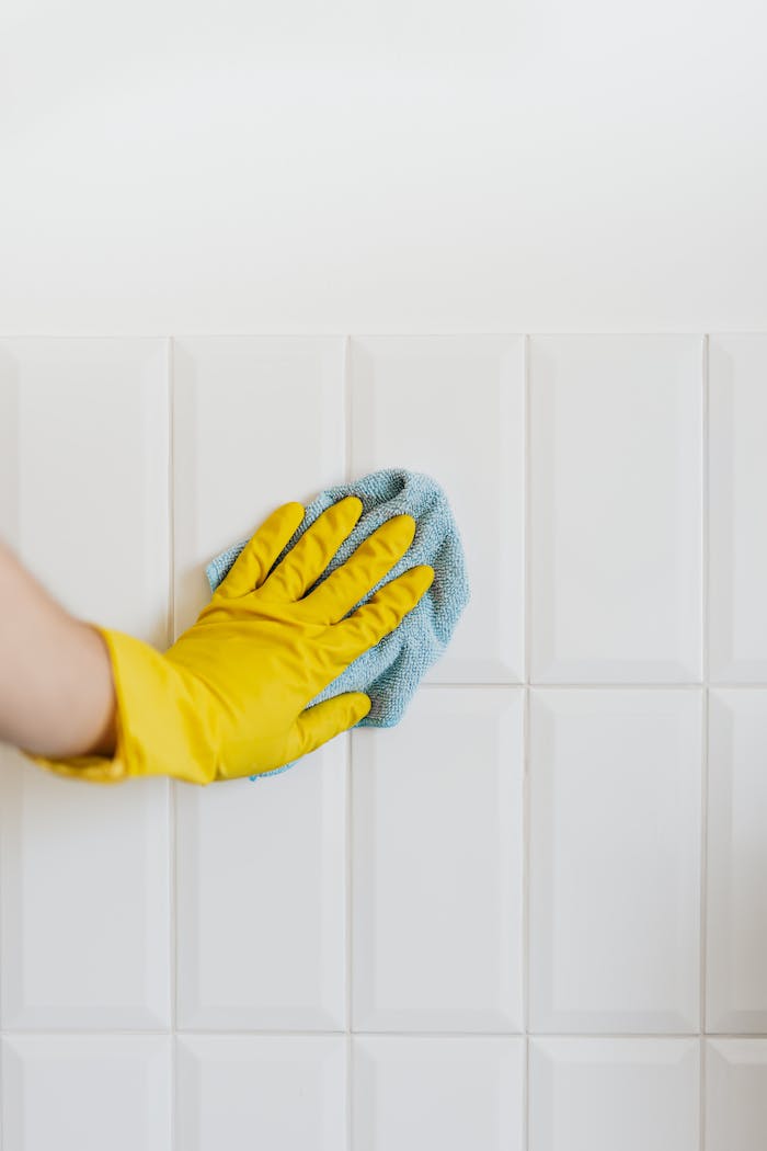 services-01 Crop unrecognizable person in yellow rubber gloves cleaning white tile wall with blue microfiber cloth in daylight