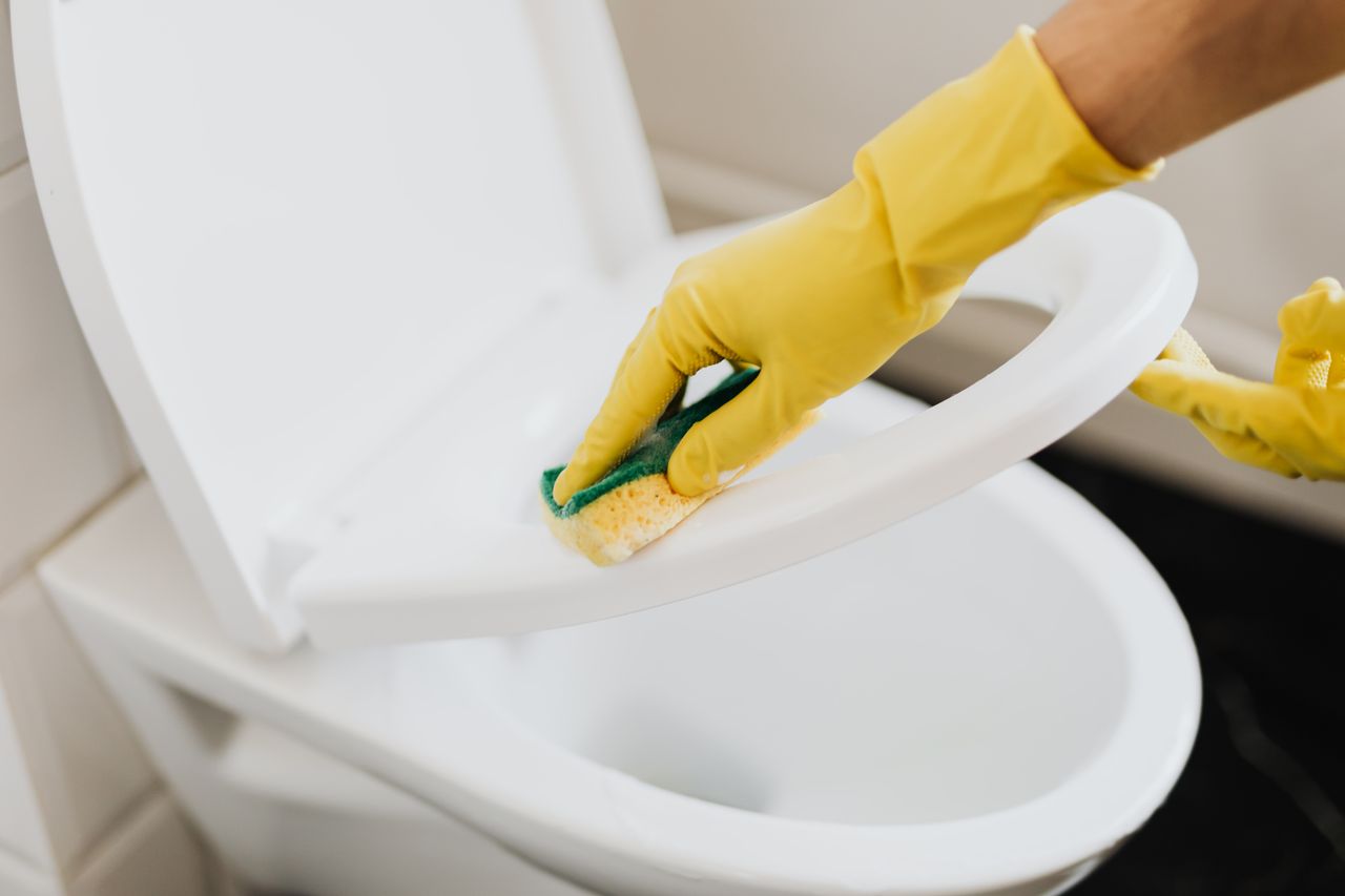 about-04 From above of crop faceless person in yellow rubber cleaning gloves cleaning plastic toilet seat properly with sponge in restroom