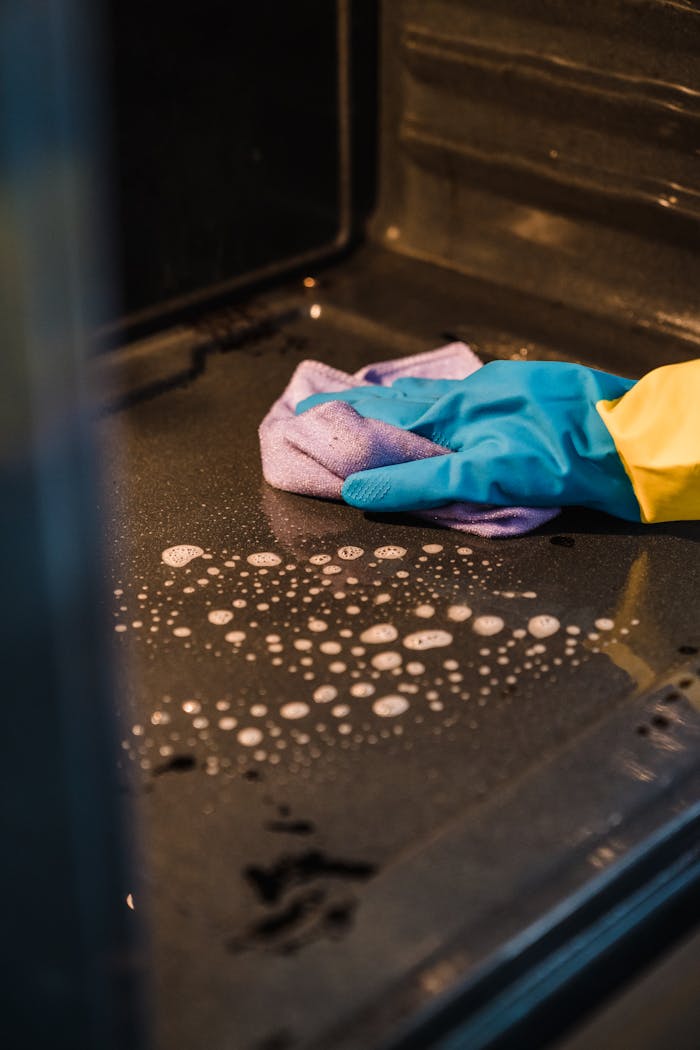 why-choose-us-02 A gloved hand cleans an oven interior using a soapy cloth for a spotless finish.