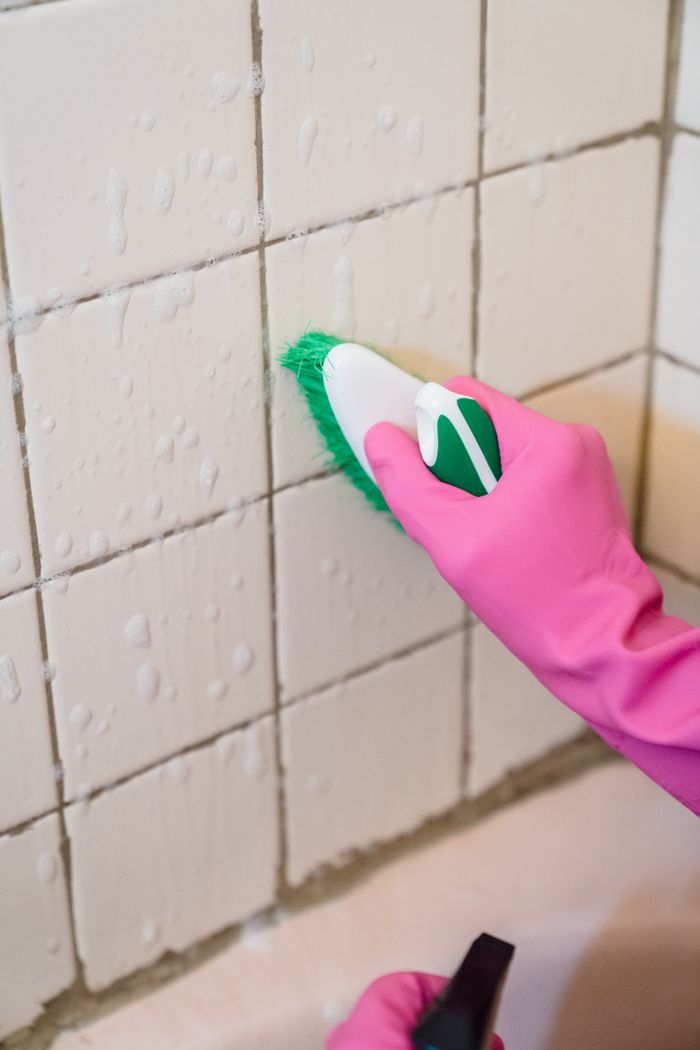 services-02 A hand in pink gloves scrubs bathroom tiles with a green brush to remove grime.