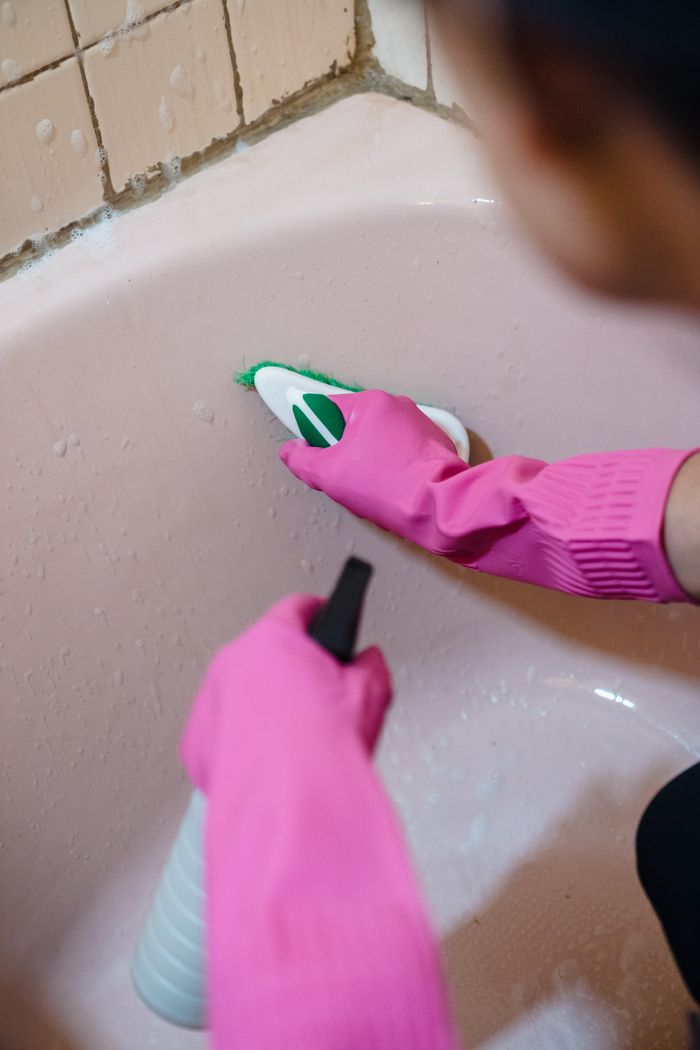 mission-02 Person using pink gloves and scrubber to clean a bathtub with tiles.